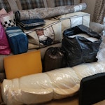 mixed household items. Hardly used single mattress, 1 disassembled swivel recliner and two foot stools, 1 rolled up king size bed topper, foam pieces, storage bag of pillows, two large sofa cushion inserts, small rug, storage bag of (bedding curtains and a few baby clothes), bag of backpacks, bag of lunch boxes, two lap trays. RG12 - removed for £200